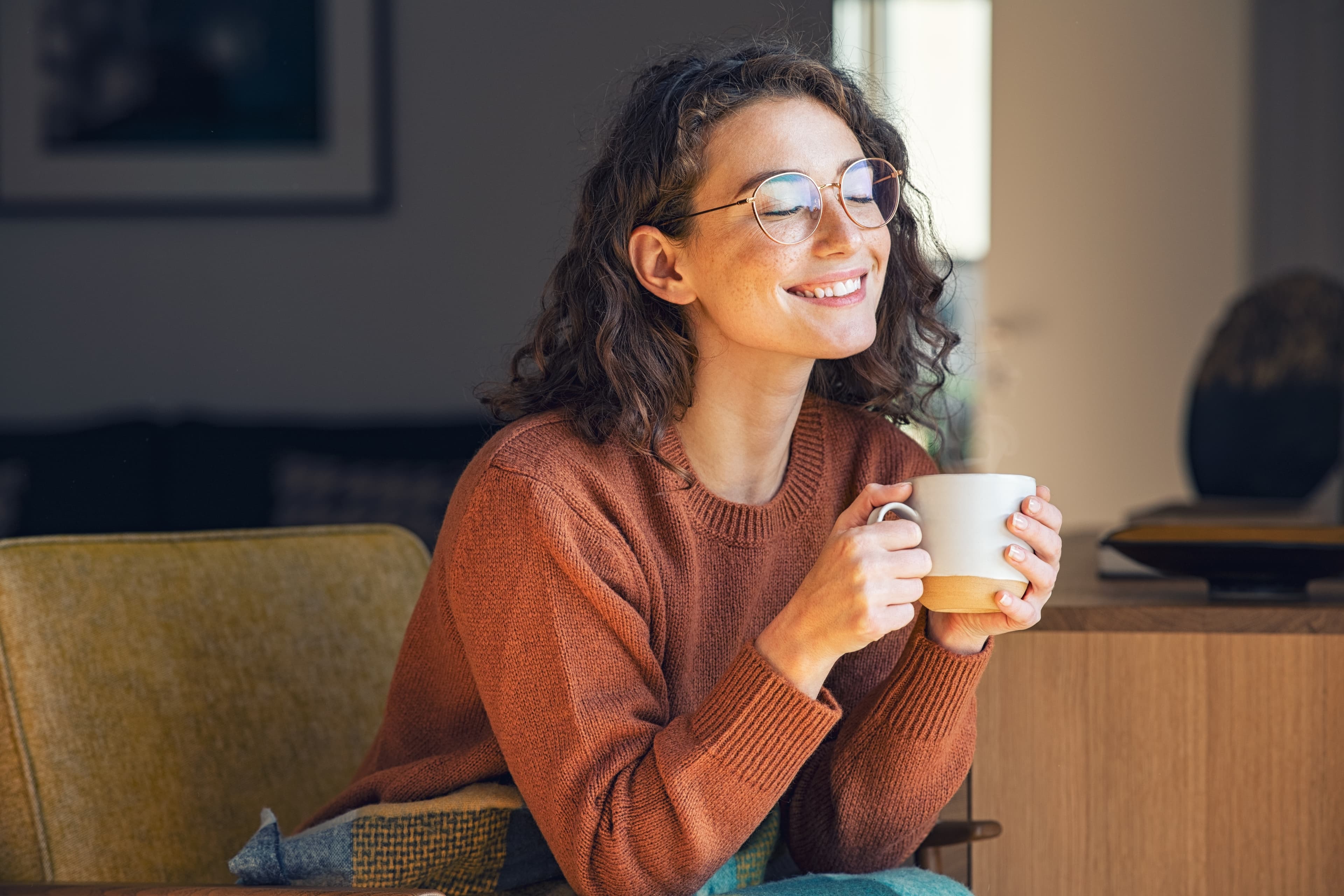 Smiling woman with glasses enjoying a cup of coffee at home