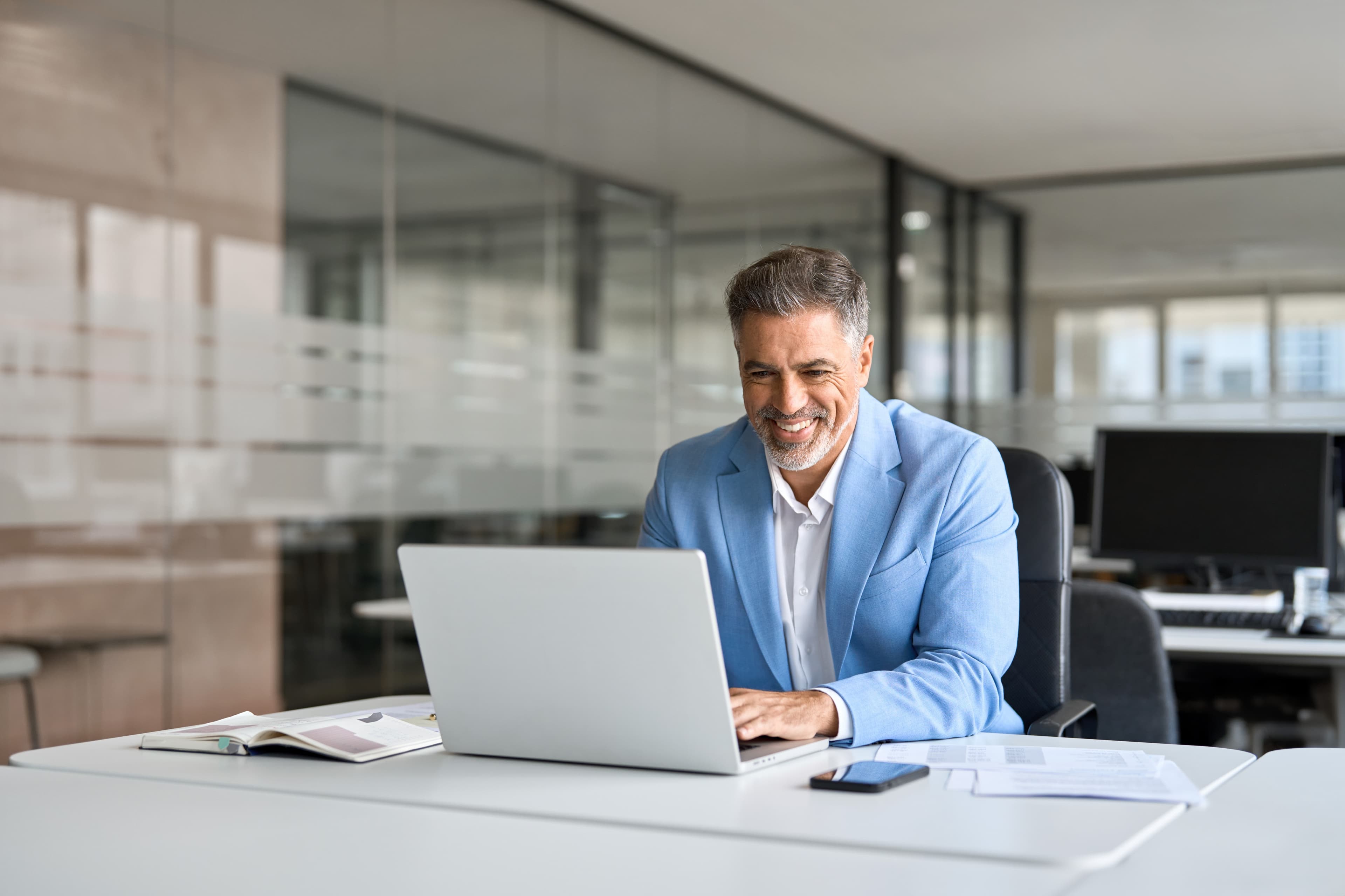 Confident businessman in a light blue suit working on a laptop in a modern office
